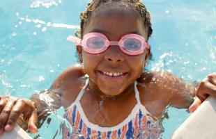 Little girl swimming in pool with goggles, smiling.