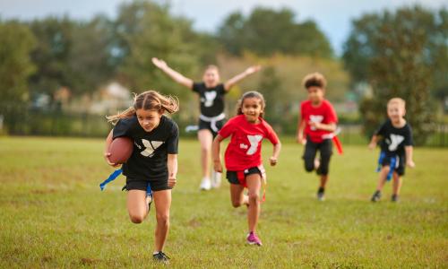 Girl running with football during YMCA flag football event