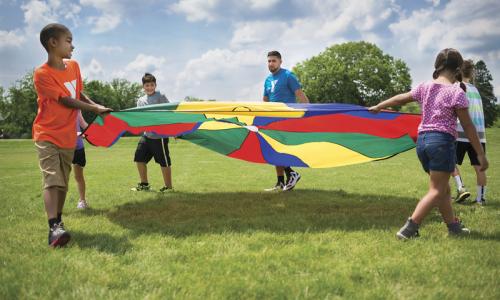 YMCA camp counselor and campers twirl a parachute