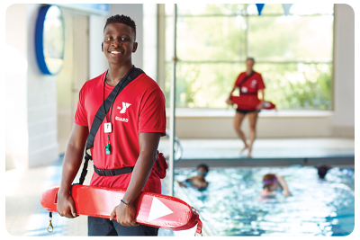 A smiling YMCA lifeguard holds a flotation device in front of a pool