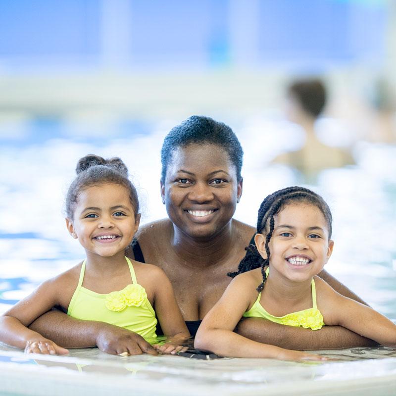 A woman and two children smile while in a pool