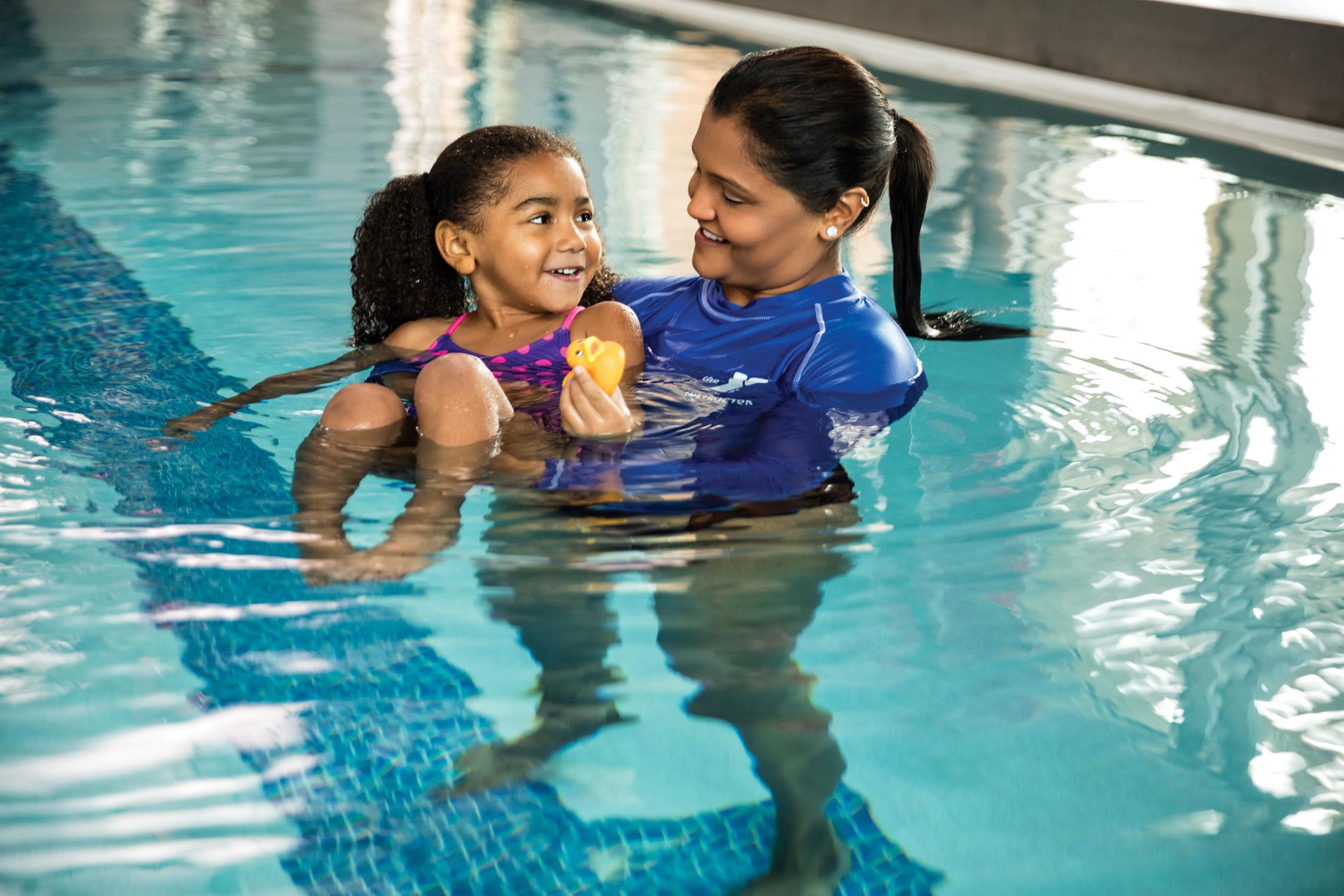 Staff person helping young girl float in the pool