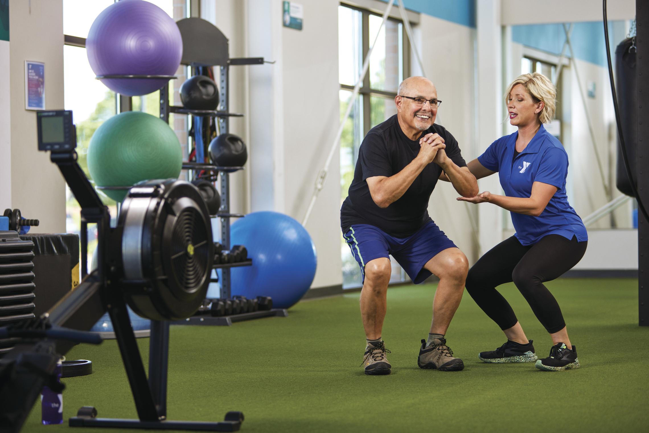 YMCA staff member assisting an older adult with fitness training in a YMCA facility.