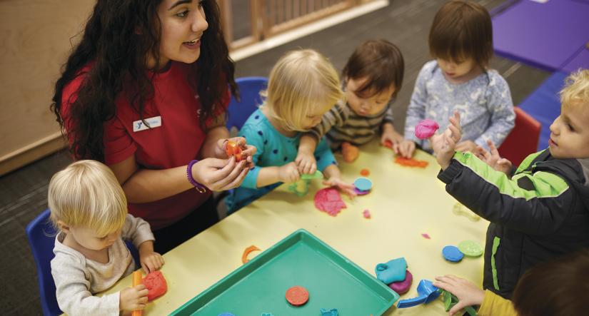 A group of preschoolers and Y staff around a table learning and playing