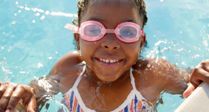 Little girl swimming in pool with goggles, smiling.