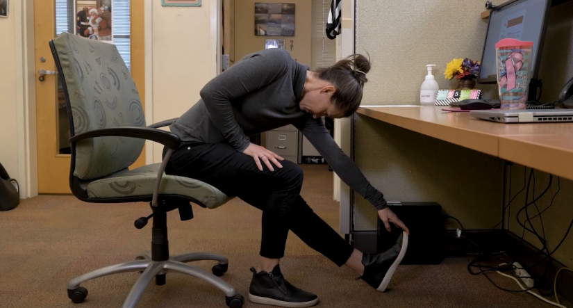 Erin Troy showing a leg stretch you can do while sitting in an office chair. 