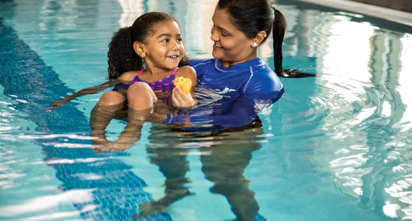 Staff person helping young girl float in the pool