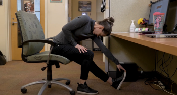 Erin Troy showing a leg stretch you can do while sitting in an office chair.